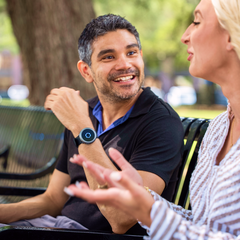 Two people having a conversation on a park bench, one wearing Sona on the wrist.